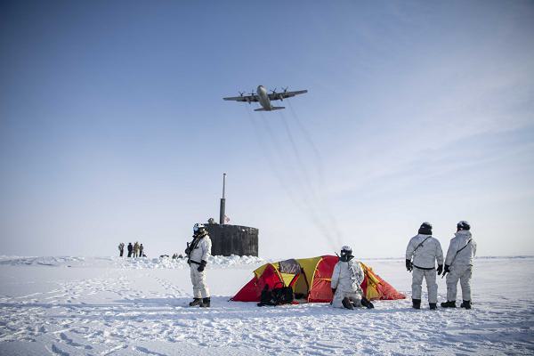 An Air Force C-130 Hercules flies over a group of Navy SEALs, Norwegian naval special operations commandos and the attack submarine USS Hampton during exercise Arctic Edge at an undisclosed location in Alaska, March 9, 2024. The exercise provides the opportunity to test a range of capabilities and response options and bolster skills in an Arctic environment. (U.S. Navy photo by Chief Mass Communication Specialist Jeff Atherton) 