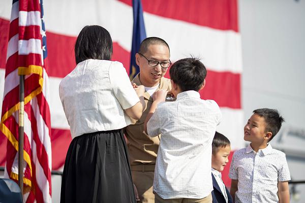 250124-N-CO542-1145Chief Electrician’s Mate Si Zhao, from Flushing, New York, is pinned by his wife and son during his commissioning ceremony on the flight deck of amphibious assault carrier USS Tripoli (LHA 7), January 24, 2025. Tripoli is an America-class amphibious assault ship homeported in San Diego. (U.S. Navy photo by Mass Communication Specialist Seaman Apprentice Eliora Sims)