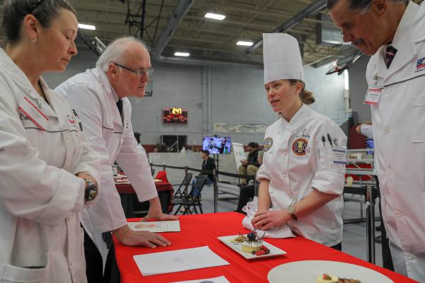 Chief Warrant Officer 2 Christine Stanley, U.S. Army Culinary Arts Team, 364th Sustainment Command (Expeditionary), listens to judge critiques after the pastry event for Team USA at the 49th Joint Culinary Training Exercise held at Fort Gregg-Adams, Virginia, March 3rd 2025. International Teams representing France, Great Britain, Germany and USA compete in various categories from pastry to hot food challenges to determine which International Team wins.