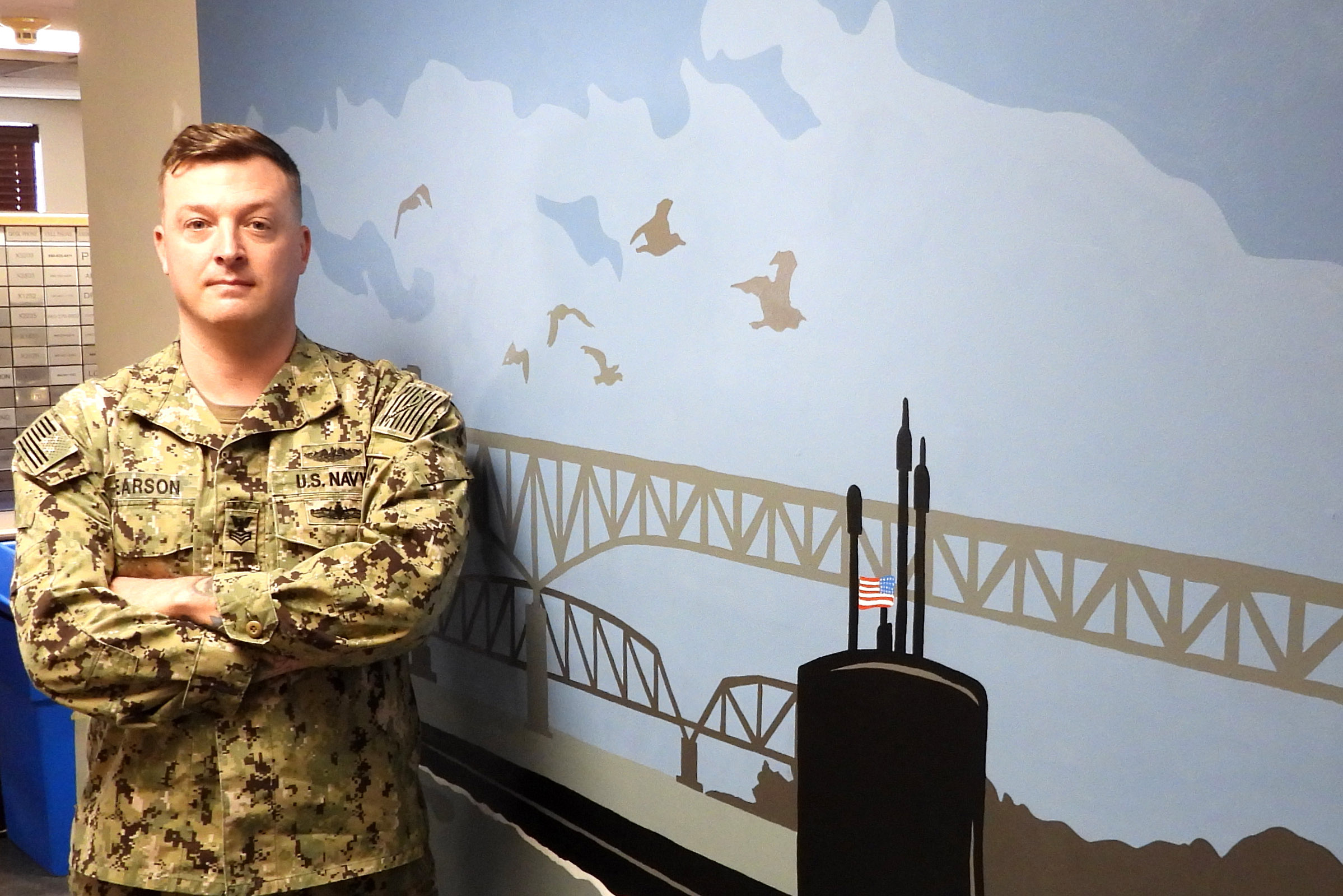 210308-N-AY957-012 GROTON, Conn. (March 8, 2021) – Petty Officer 1st Class Jamie Pearson, a Machinist’s Mate (Auxiliary) assigned to Naval Submarine Support Facility New London, stands in front of a mural he painted for his command’s conference room. Pearson has been moonlighting as an artist on and off base in the Groton community since 2014. (photo by Chief Petty Officer Joshua Karsten/RELEASED)