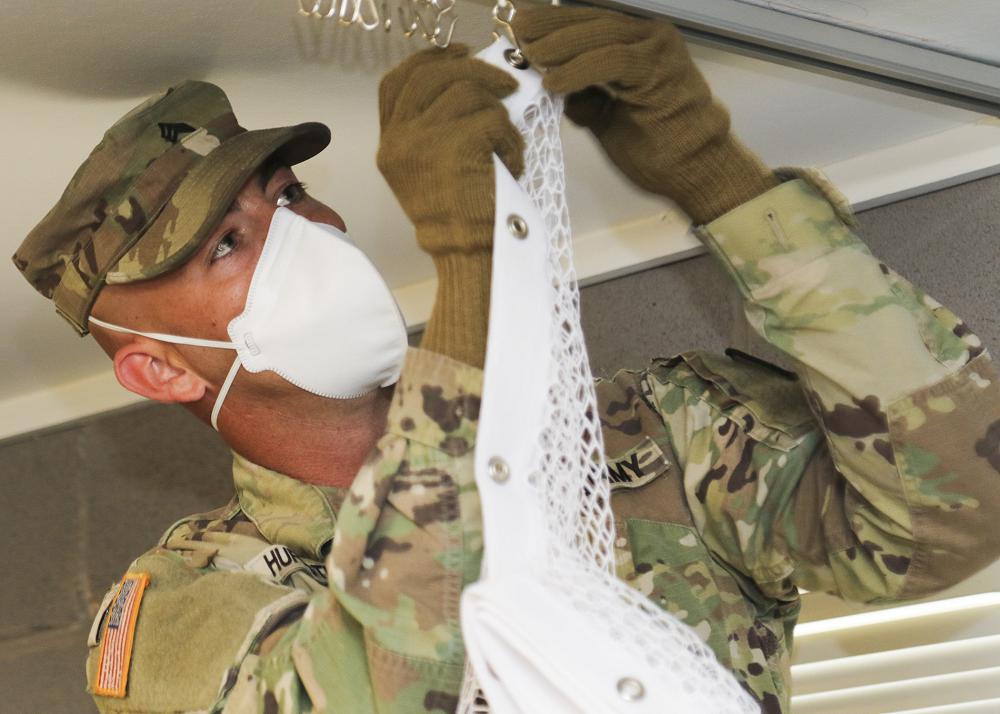 Texas Army Sgt. Keith Huffstuttler, a team leader with Task Force 176’s 840th Engineering Mobility Augmentation Company, installs curtains to separate beds in Camp Swift barracks to adapt them into medical isolation support facilities in Bastrop, Texas, April 17, 2020. The isolation facility is for Soldiers, Airmen and State Guardsmen suspected of having COVID-19. (Photo by Staff Sgt. Michael Giles)