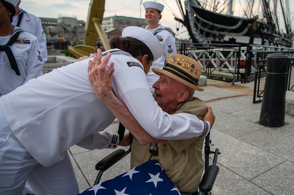 BOSTON (July 16, 2021) Retired Army Staff Sgt. Jake Larson embraces Seaman Nicole Gonzalez, from Manteca, California, in front of USS Constitution. Larson is a World War II veteran who landed at Omaha Beach on D-Day and fought at the Battle of the Bulge. Constitution is the world’s oldest commissioned warship afloat, and played a crucial role in the Barbary Wars and the War of 1812, actively defending sea lanes from 1797 to 1855. During normal operations, the active-duty Sailors stationed aboard Constitution provide free tours and offer public visitation to more than 600,000 people a year as they support the ship’s mission of promoting the Navy’s history and maritime heritage and raising awareness of the importance of a sustained naval presence. Constitution was undefeated in battle and destroyed or captured 33 opponents. The ship earned the nickname of Old Ironsides during the war of 1812 when British cannonballs were seen bouncing off the ship’s wooden hull. (U.S. Navy Photo by Mass Communication Specialist 2nd Class Grant Grady)                      