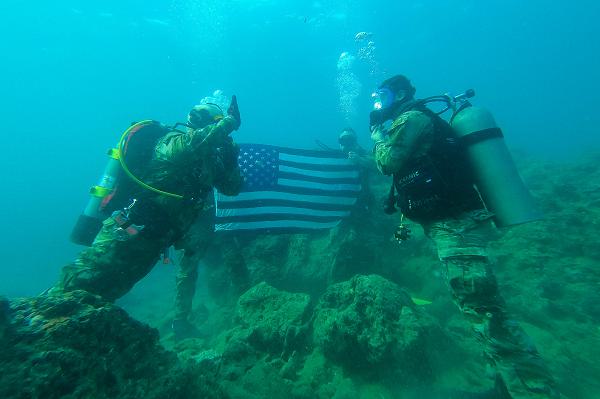 Amidst the serene backdrop of Okinawa's coastal waters, Maj. Robert S. Bourgeau and Sgt. 1st Class Corey O. Tomasich, accompanied by Capt. Erik McDowell and Capt. Timothy Robinson, prepare to descend for a significant underwater reenlistment. This image captures a moment of camaraderie and solemn preparation as these members of the 10th Support Group gear up, reflecting their deep commitment to service. The ceremony underlines the harmonious blend of professional military duties with the personal pursuits of its members, all set against the expansive blue of the Pacific.
