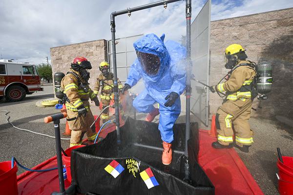 U.S. Air Force Airman 1st Class Seth Dixon (left) and Airman Joseph Ransdell (right), 355th Civil Engineer Squadron fire protection specialists, decontaminate Senior Airman Ronald Cataldo (middle), 355th CES Explosive Ordnance Disposal team member, during a simulated chemical, biological, radiological and nuclear attack at Davis-Monthan Air Force Base, Arizona, Aug. 21, 2024. The fire Airmen set up the decontamination zone in order to dry and wet scrub those exposed to the unidentified substance. (U.S. Air Force photo by Senior Airman Paige Weldon)