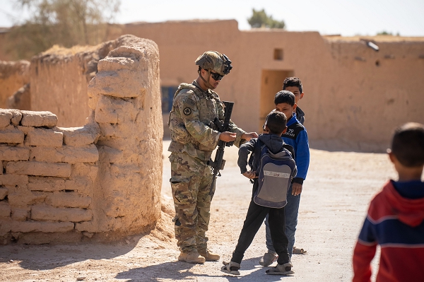 A U.S. Army Soldier from Charlie Company, 1st Battalion, 181st Infantry Regiment, 44th Infantry Brigade Combat Team, assigned to Combined Joint Task Force - Operation Inherent Resolve, gives candy to local children during a dismounted patrol through a village in Northeast Syria. (U.S. Army photo by Staff. Sgt. Emma Scearce)