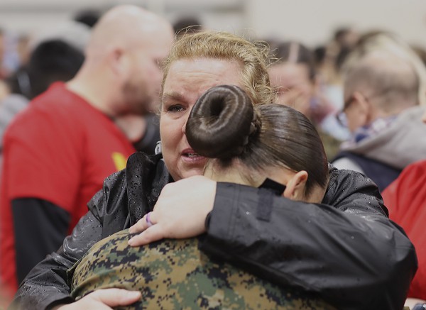 Paris Island, S.C. (August 8, 2022): In this photo by Corporal Samuel Fletcher, Marines embrace loved ones during Family Day at Marine Corps Recruit Depot, Parris Island, South Carolina. The event allows newly minted Marines the chance to reconnect with their families before graduation day.  This Marine went through several intense phases of physical and emotional training to earn the right to wear the eagle, globe, and anchor of the U.S.M.C.