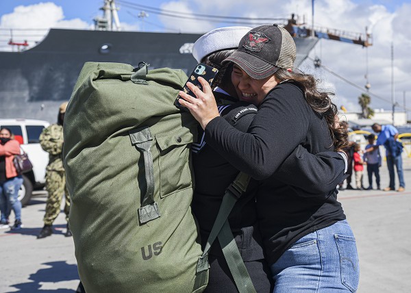 San Diego, CA. (August 14, 2022): In this photo by Specialist 3rd Class Melvin Fatimehin, a sailor hugs a family member after completing a seven-month deployment aboard the Harpers Ferry-Class Dock Landing Ship USS Pearl Harbor.  Based at Naval Base San Diego, the Pearl Harbor just returned from operations in the Indo-Pacific region in support of America’s 3rd, 5th, and 7th Fleets. With a crew of 24 officers and 328 enlisted, the Pearl Harbor’s mission is to transport and launch amphibious craft and their crews to conduct assault landings.