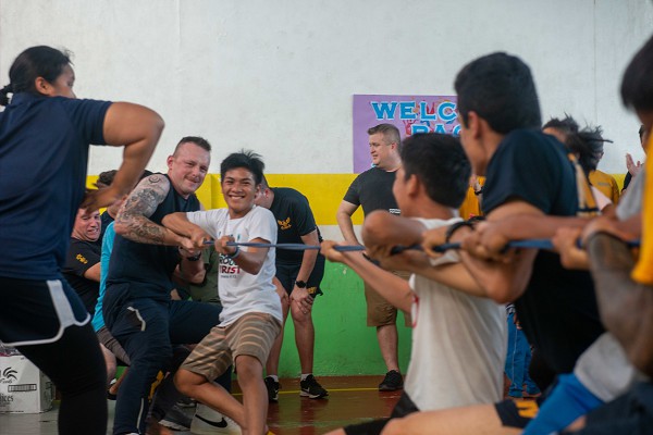 Manila, Philippines. (October 15, 2022): In this photo by Petty Officer 2nd Class Michael Jarmiolowski, Electronics Technician 3rd Class Ian Reynolds, left, from Virginia Beach, Virginia, goes hands on in a tug of war with children at Gentle Hands Orphanage as part of the Navy’s community relations effort. Sailors volunteered for the event to play games and create hand-drawn paintings with over 100 children. The Sailors are assigned to the guided-missile cruiser USS Chancellorsville, part of the Ronald Reagan Carrier Group.  Young, enthusiastic Sailors like these often make the best ambassadors for our country.