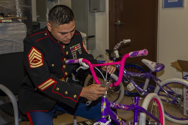 Andersen Air Force Base, Guam. (December 14, 2021): In this photo by Corporal Andrew King, Gunnery Sergeant Rubin Tan, the Marine Corps Base Camp Blaz Communications and Operations Chief, assembles a donated bike as part of the Marine’s Toys for Tots campaign to bring the joy of Christmas to underprivileged children. Ironically, Marines like Gunny Tan and thousands like him will be far from home this holiday season.