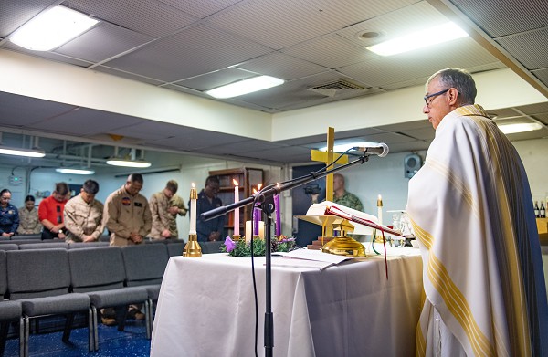 Gulf of Aden. (December 24, 2021): In this photo by Petty Officer 2nd Class Jonathan Word, Lieutenant Paul Guzman, a Catholic Chaplain deployed to Camp Lemonnier, Djibouti, performs Christmas Eve Mass for U.S. Sailors and Marines aboard the amphibious assault ship USS Essex. For thousands of American servicemembers, the holidays can be a lonely time serving far from loved ones at Christmas. Military clergy, of all denominations, are there to counsel young troops to help them cope with their first holiday season away from home. 